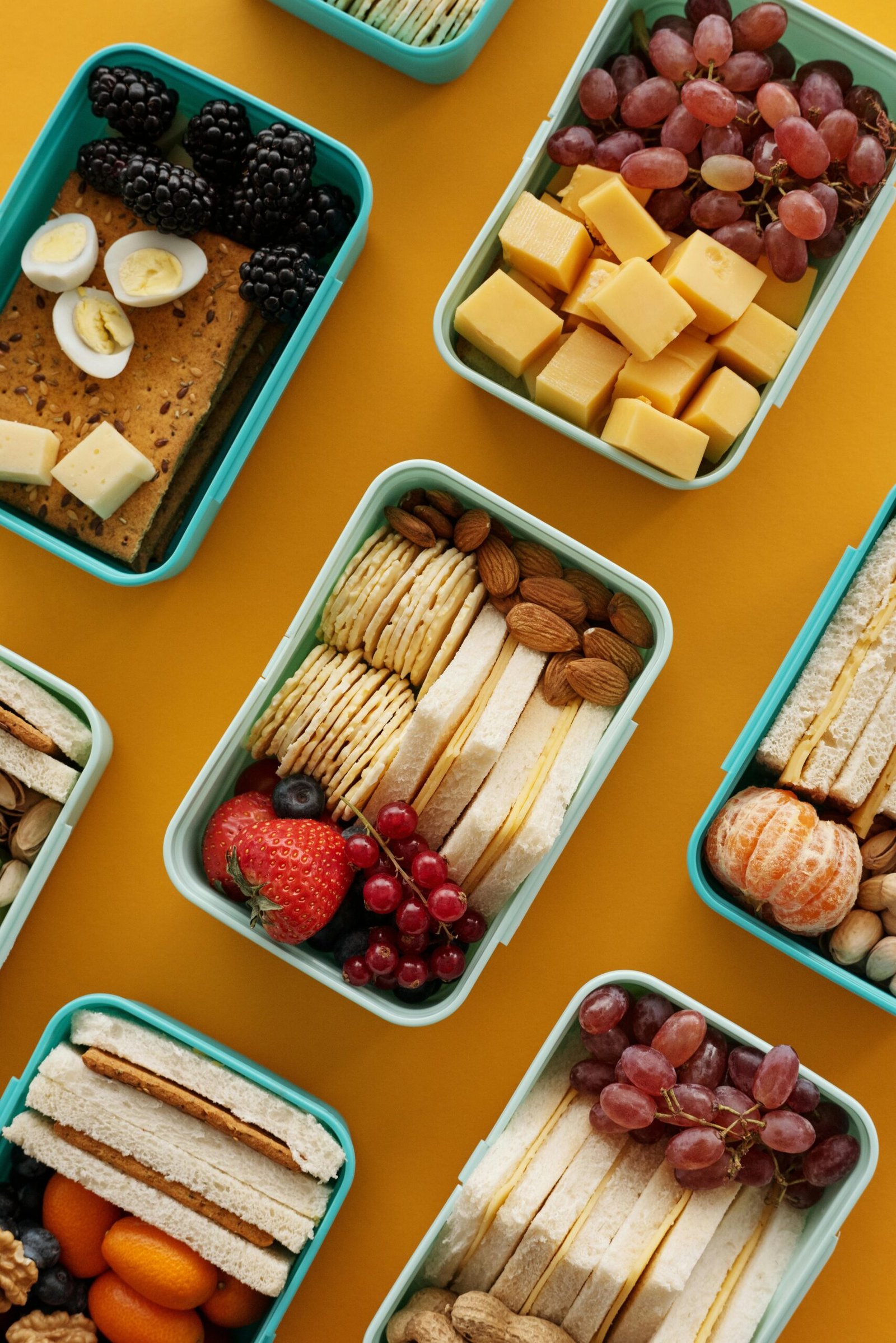 Assorted lunch boxes with snacks, fruits, and cheese on a vibrant yellow background.
